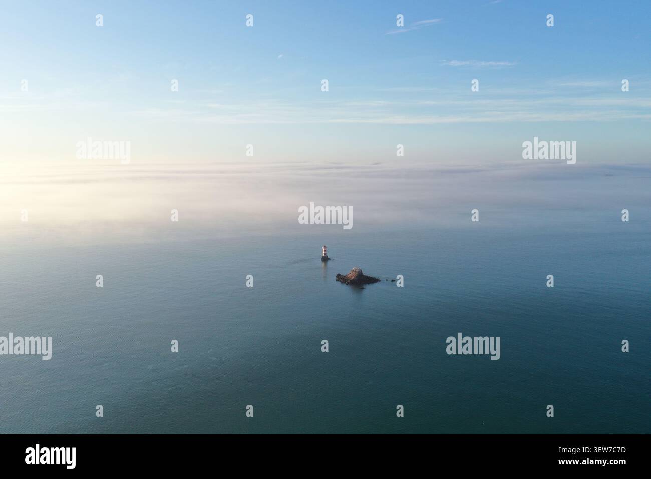 Una foto con un drone si affaccia lungo una spiaggia sabbiosa e un mare calmo verso un lontano e torbido skyline della città, con nuvole frammentate che si riflettono sulla superficie dell'acqua e un fe Foto Stock