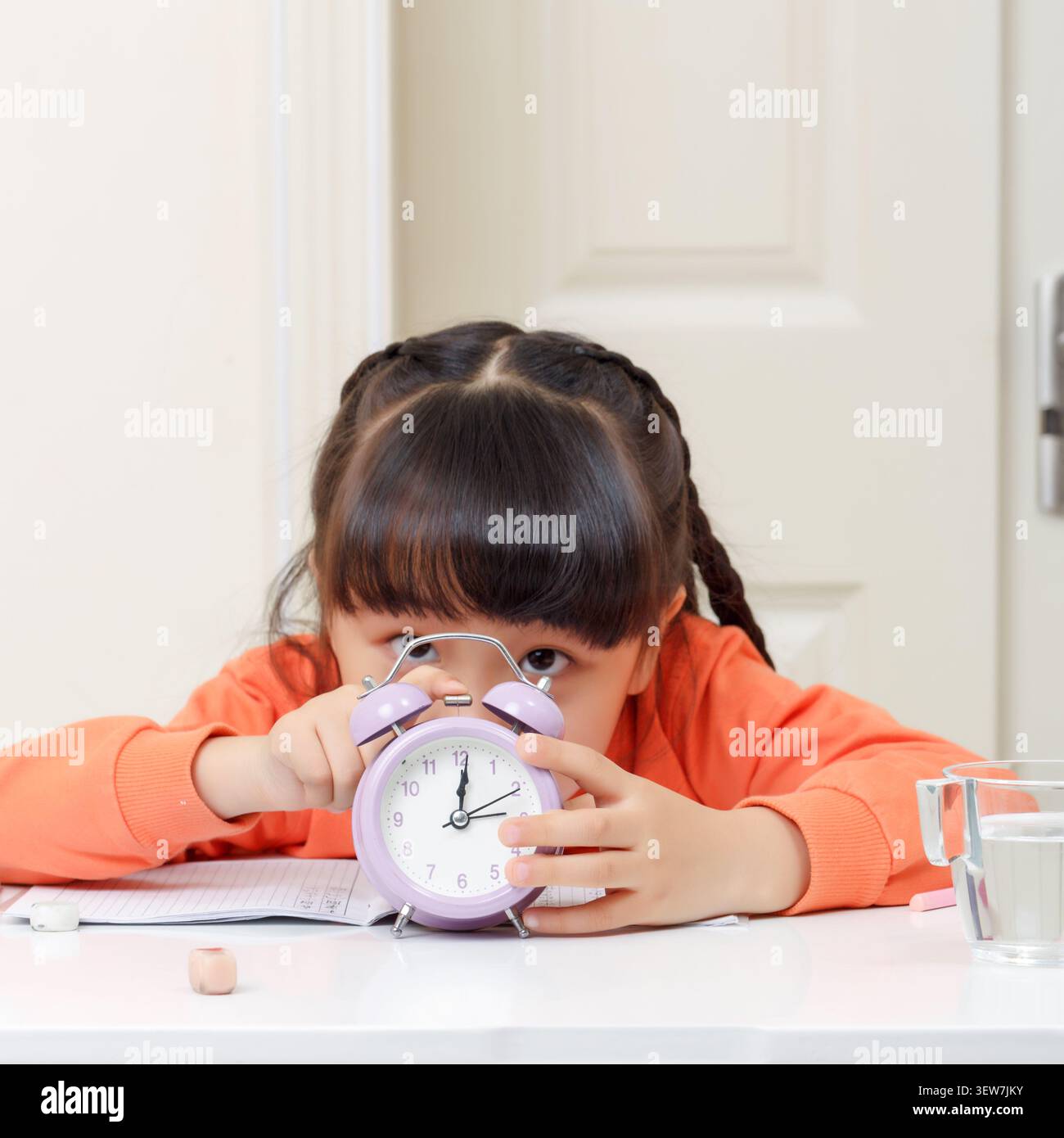 Studentessa asiatica stanca sdraiata sulla scrivania con sveglia, concetto di stanchezza, stress da studio e mancanza di sonno Foto Stock