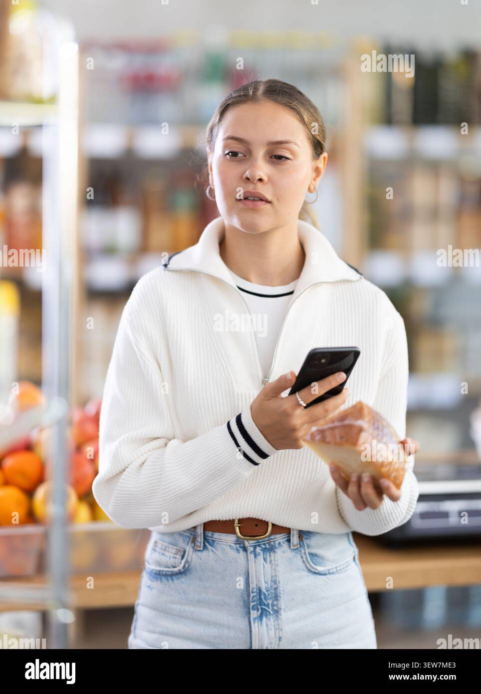 L'acquirente donna esegue la scansione del codice QR sull'etichetta del formaggio nel negozio di alimentari Foto Stock