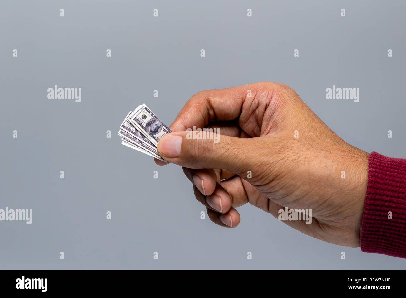 Primo piano di una mano umana che tiene minuscole banconote in dollari USA in miniatura su uno sfondo grigio. Inflazione, basso potere d'acquisto, valore decrescente del denaro Foto Stock