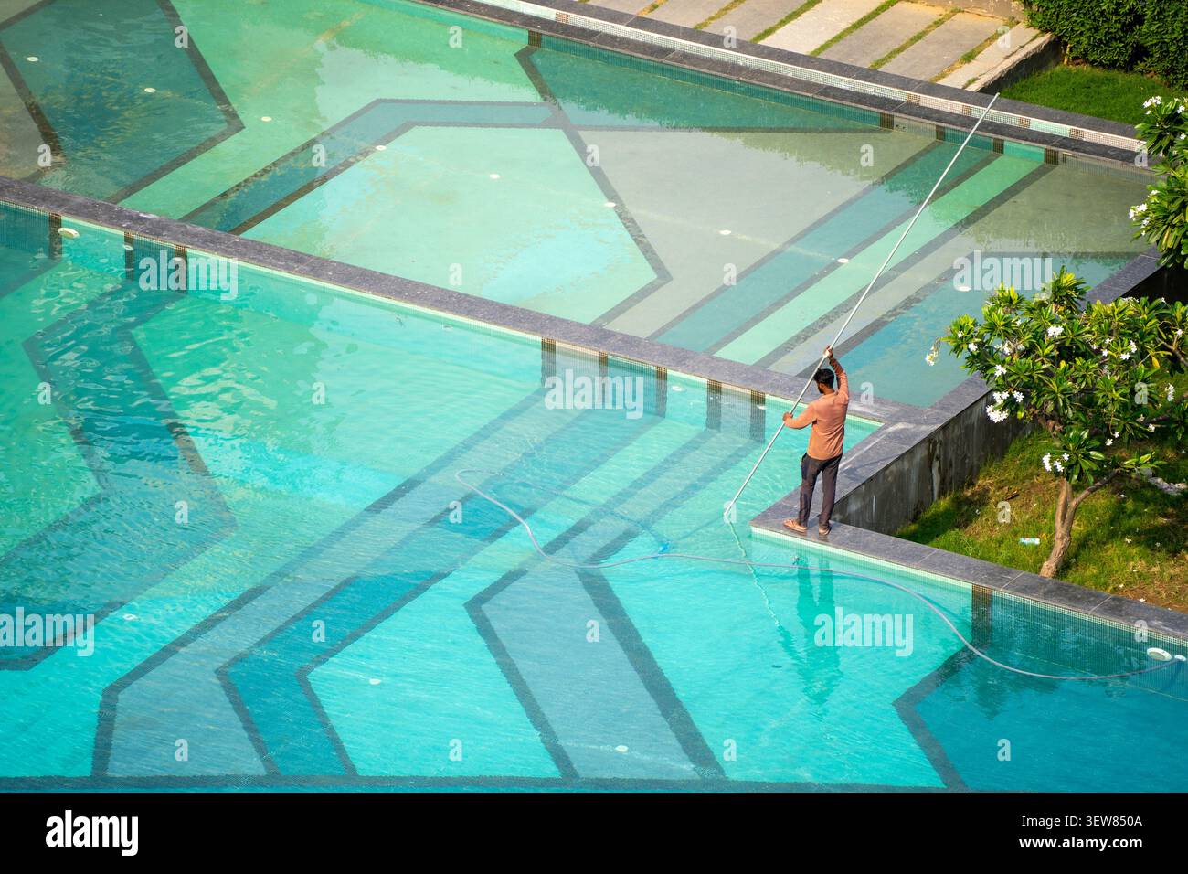 Un operatore di manutenzione che pulisce una grande piscina in un condominio di lusso a Gurgaon, evidenziando la cura della proprietà e il tempo libero Foto Stock