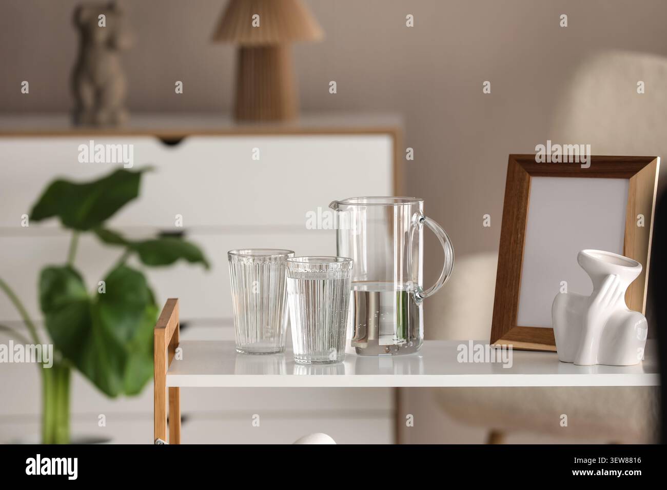Caraffa di vetro e bicchieri con acqua sul tavolo in interni moderni Foto Stock