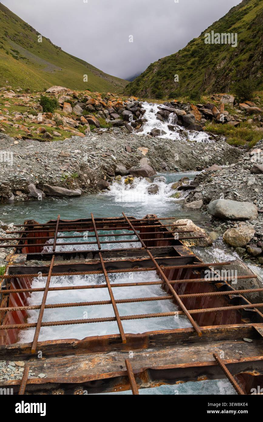 Griglia di armatura in acciaio di presa di acqua idroelettrica sul torrente di montagna in Kirghizistan durante il giorno estivo piovoso. Foto Stock