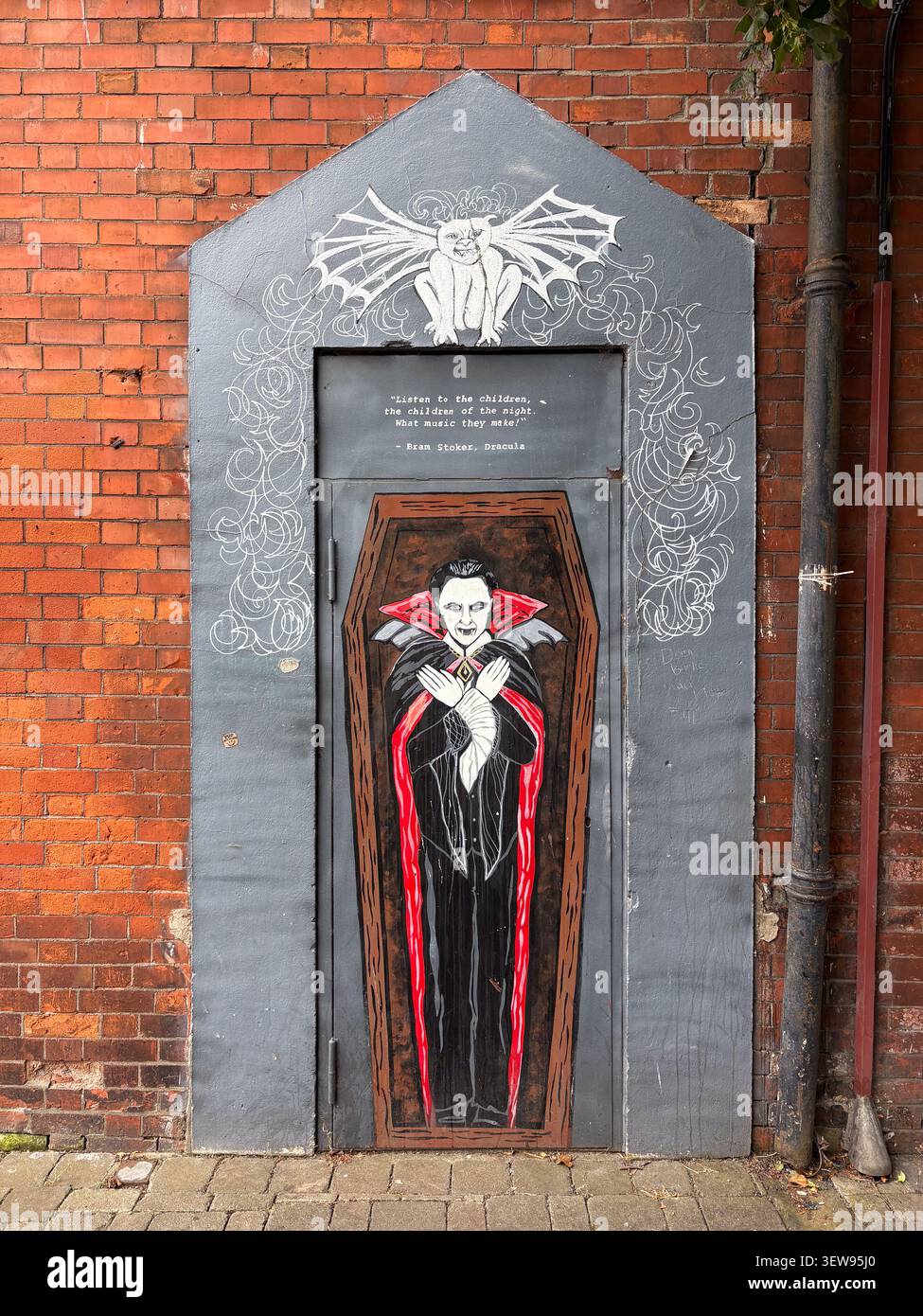 Murale di Street art del Conte Dracula in una bara dipinta su una porta grigia incastonata in un muro di mattoni rossi, con una citazione letteraria di Bram Stoker. Foto Stock