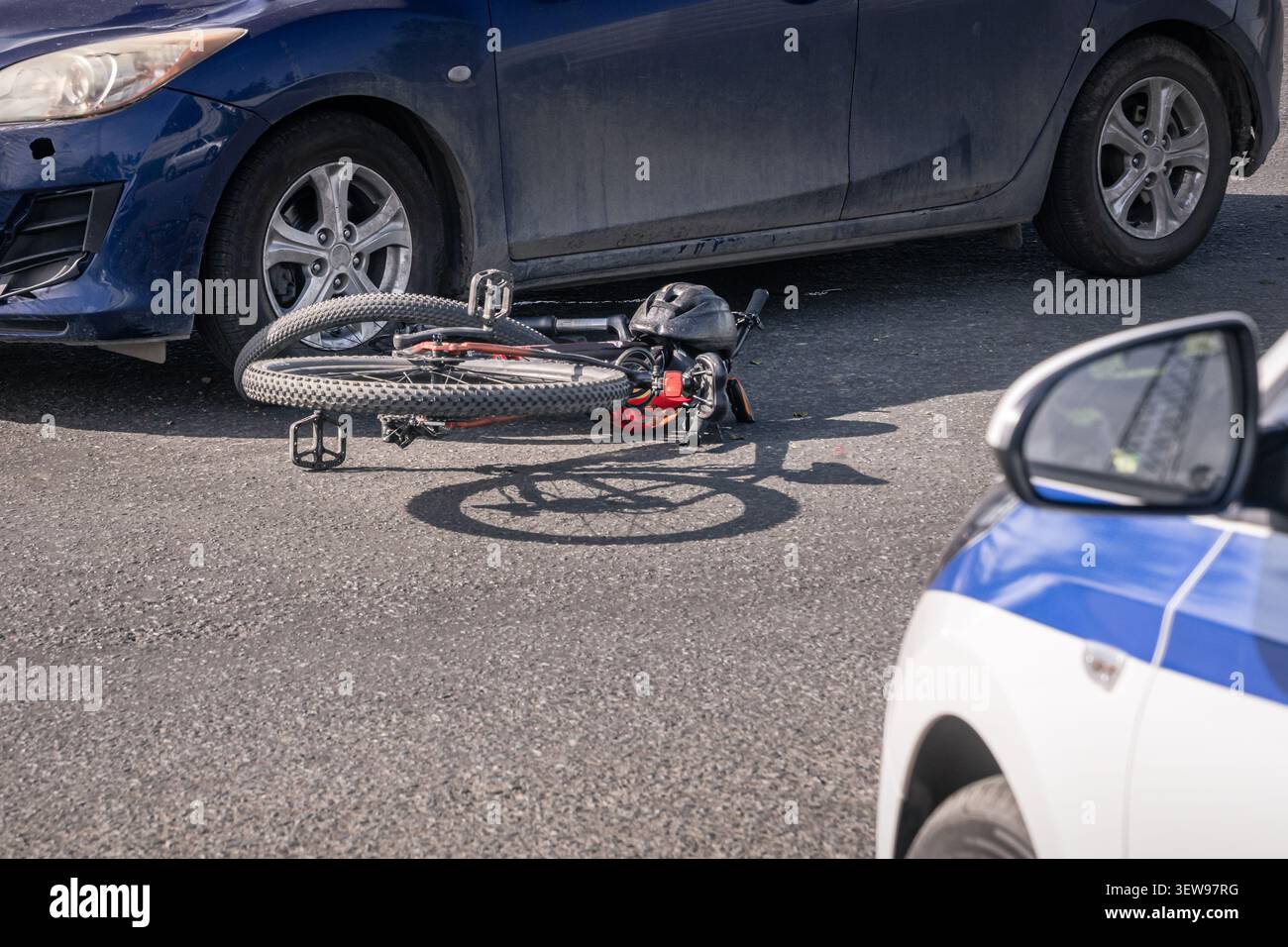 Bicicletta danneggiata stesa sulla strada dopo una collisione con un'auto mentre un'auto della polizia assiste alla scena dell'incidente. Immagine editoriale che mostra un'accisa di ciclisti Foto Stock