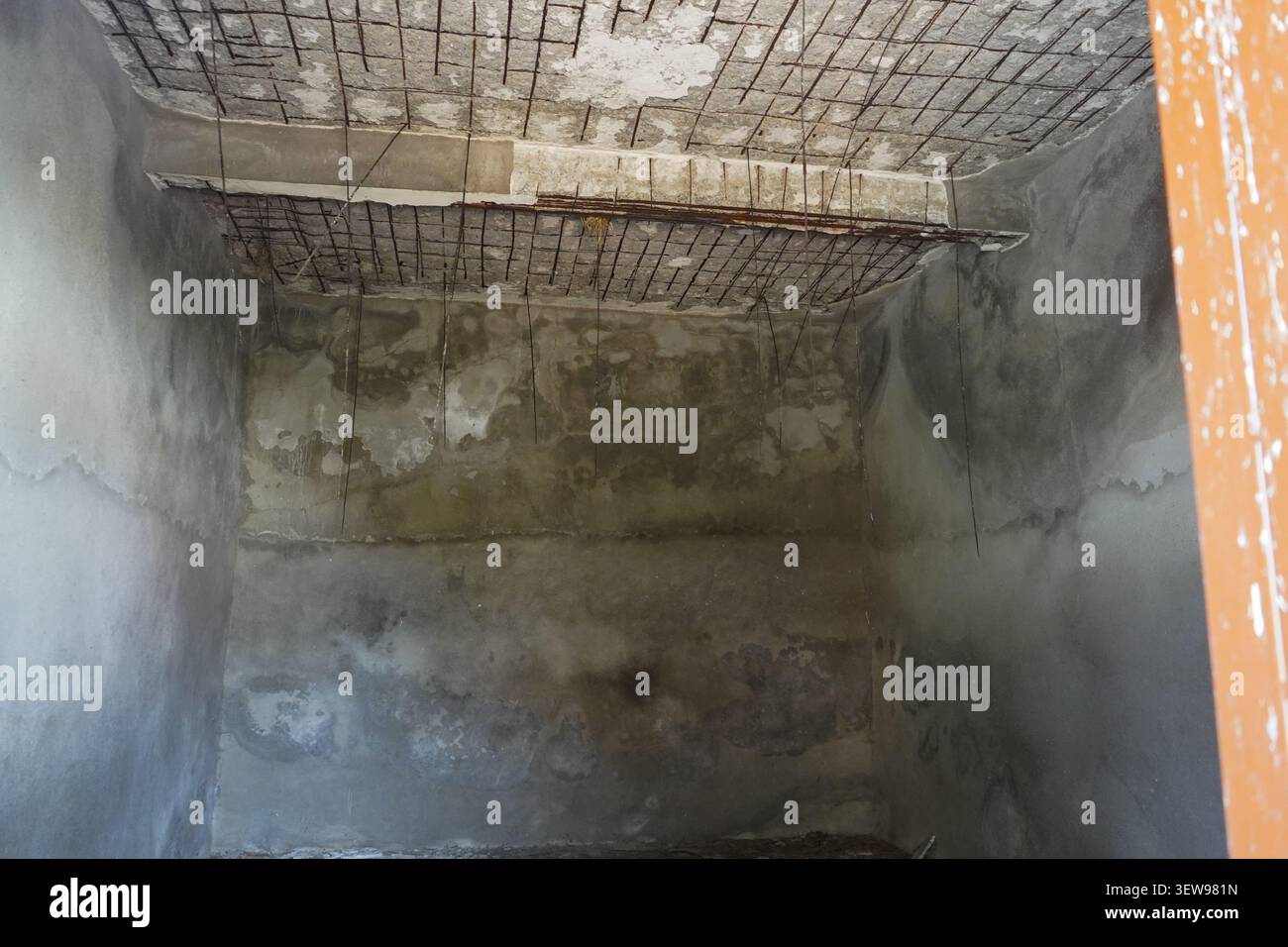 L'interno di una stanza in cemento scura e abbandonata con pareti gravemente macchiate e armature in ferro esposte pericolosamente appese al soffitto. Foto Stock