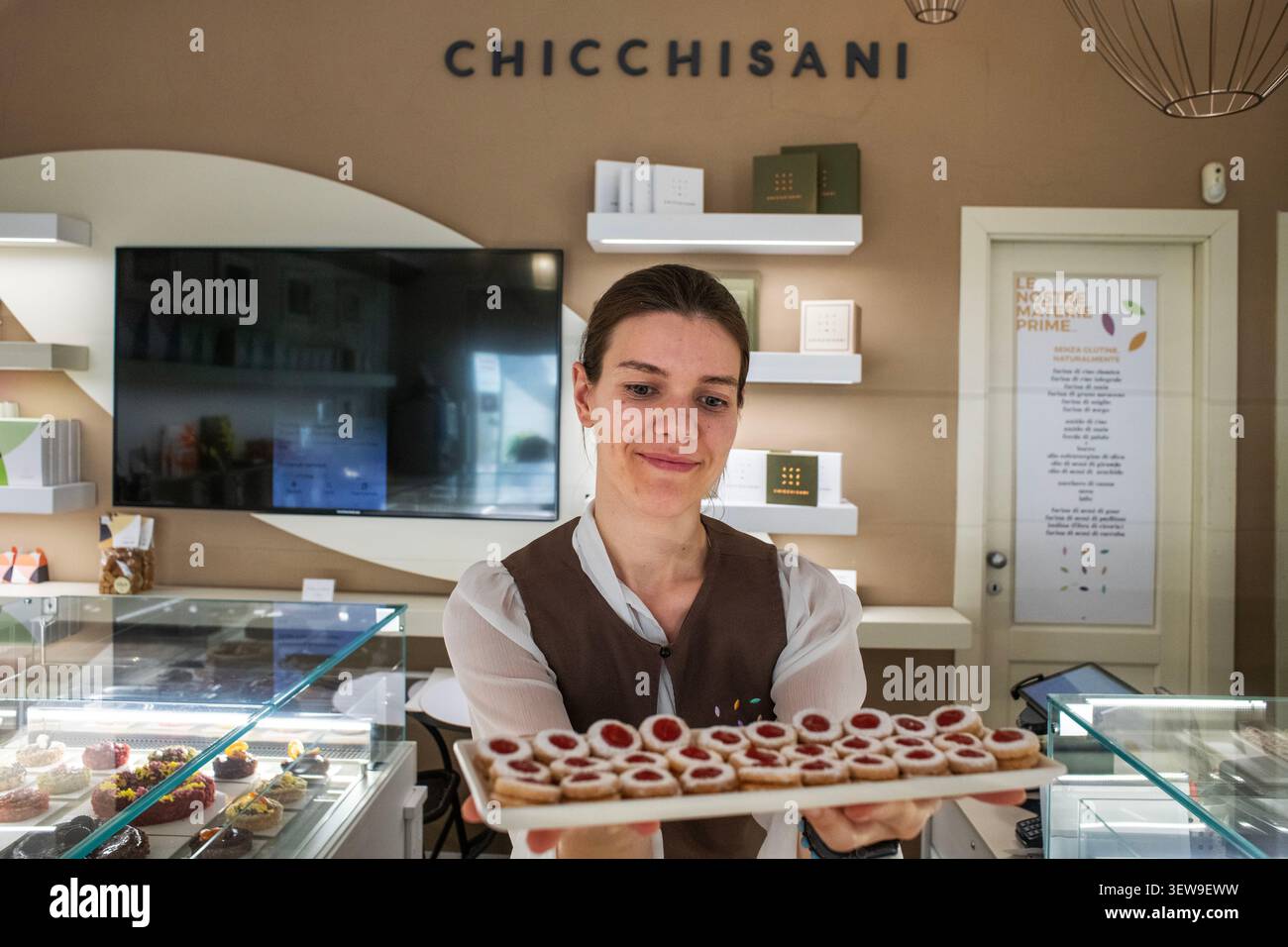 Un assistente di negozio sorridente che presenta un vassoio di marmellate appena sfornate all'interno della pasticceria Chicchisani di Torino, Italia. Situato in una città rinomata Foto Stock