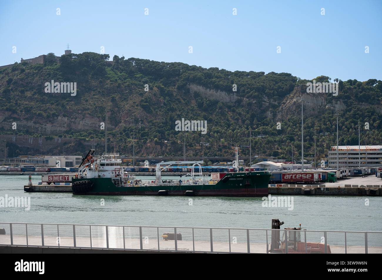 La nave da carico Green Cadiz attraccò al porto industriale di Barcellona, con container, camion da trasporto e Montjuic Mountain con il suo castello nel bac Foto Stock