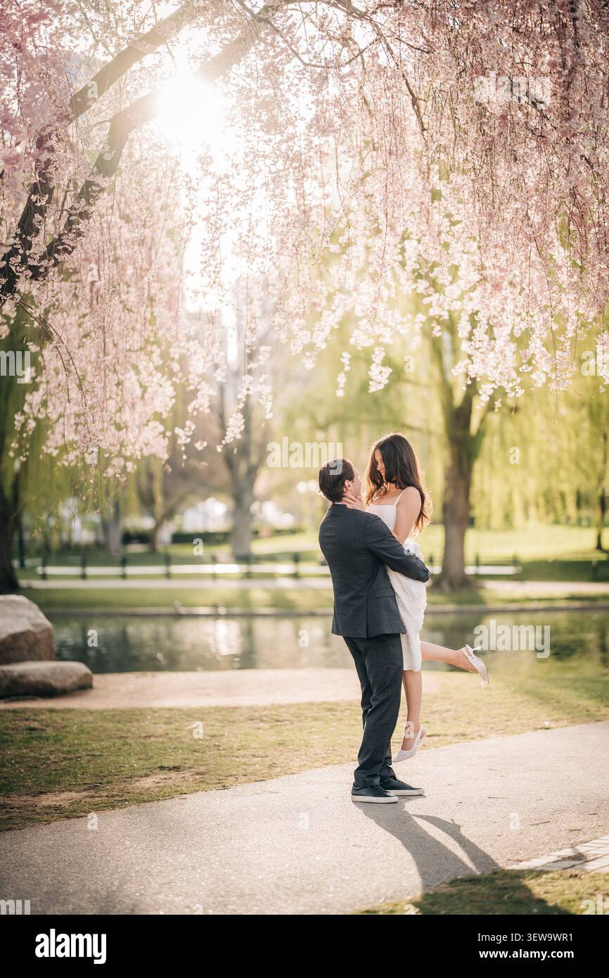 L'uomo tiene la donna sotto i fiori di ciliegio rosa Foto Stock