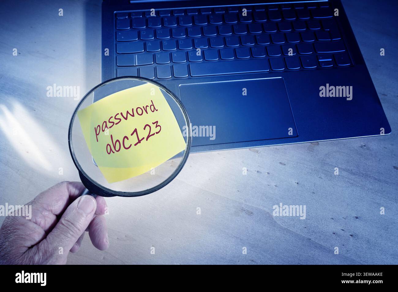 Con una lente d'ingrandimento che trova la password non sicura su un foglietto adesivo attaccato alla tastiera di un notebook, protezione insufficiente contro il furto di dati, Foto Stock