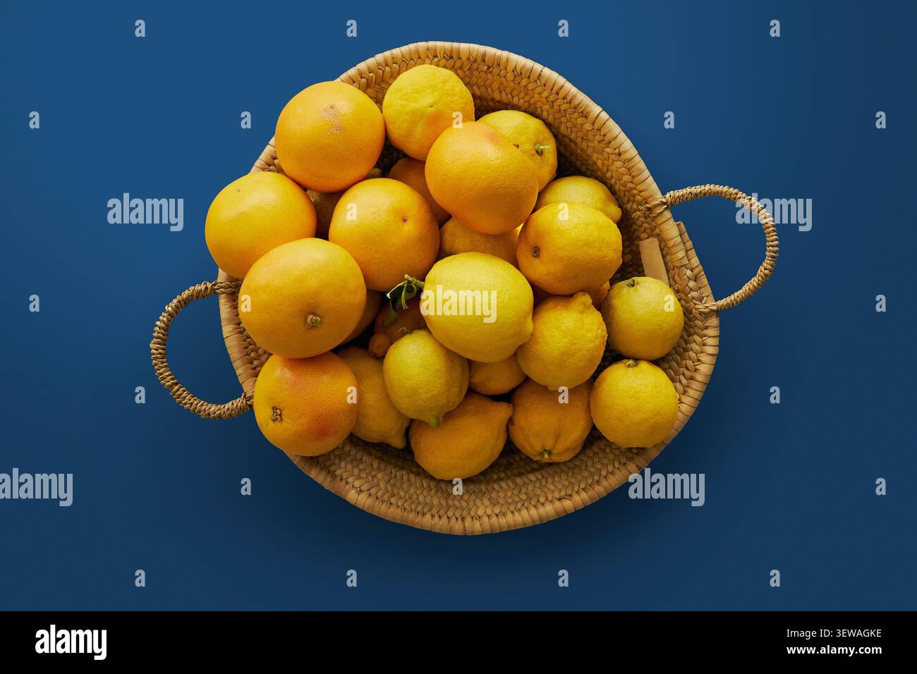 Ammira dall'alto la natura morta dei limoni e dei pompelmi in un cesto intrecciato su sfondo blu Foto Stock