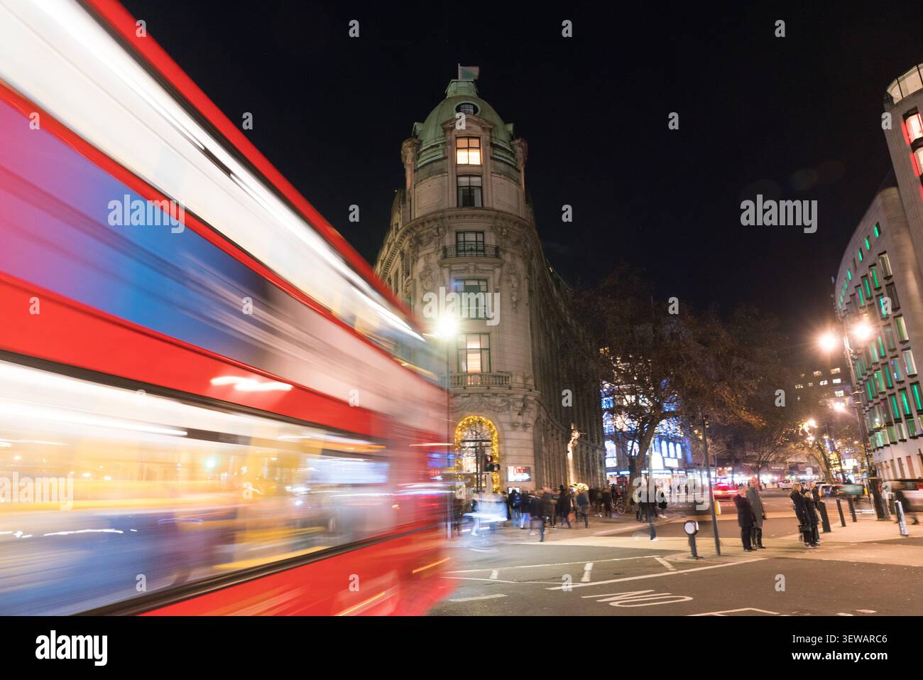 Un autobus rosso a due piani passa davanti all'iconica cupola di One Aldwych, catturando l'energia del West End di Londra di notte. Foto Stock