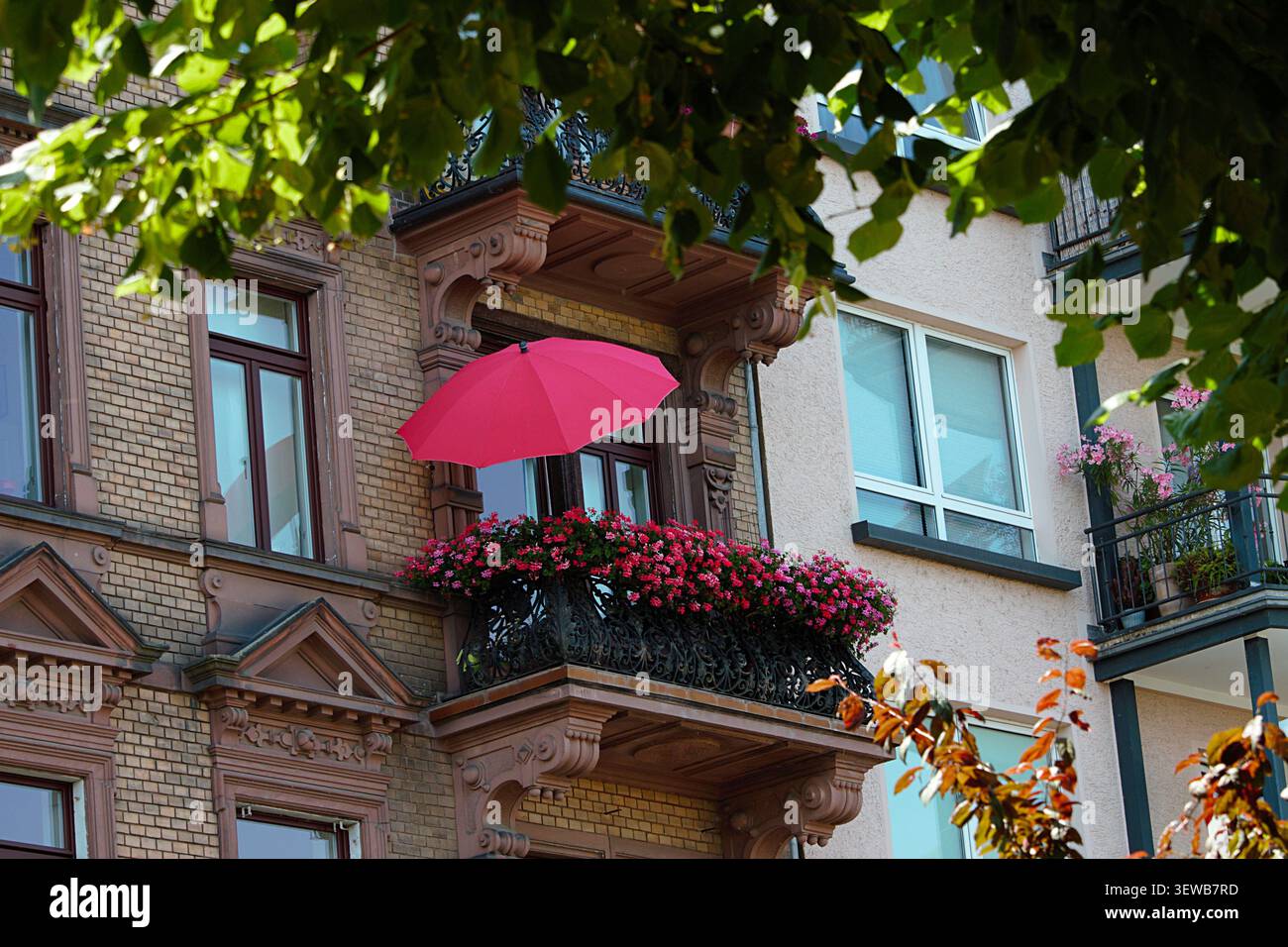 Magonza, Renania-Palatinato, Germania - 25 giugno 2026: Balcone fiorito con ombrello rosso sull'edificio storico. Foto Stock