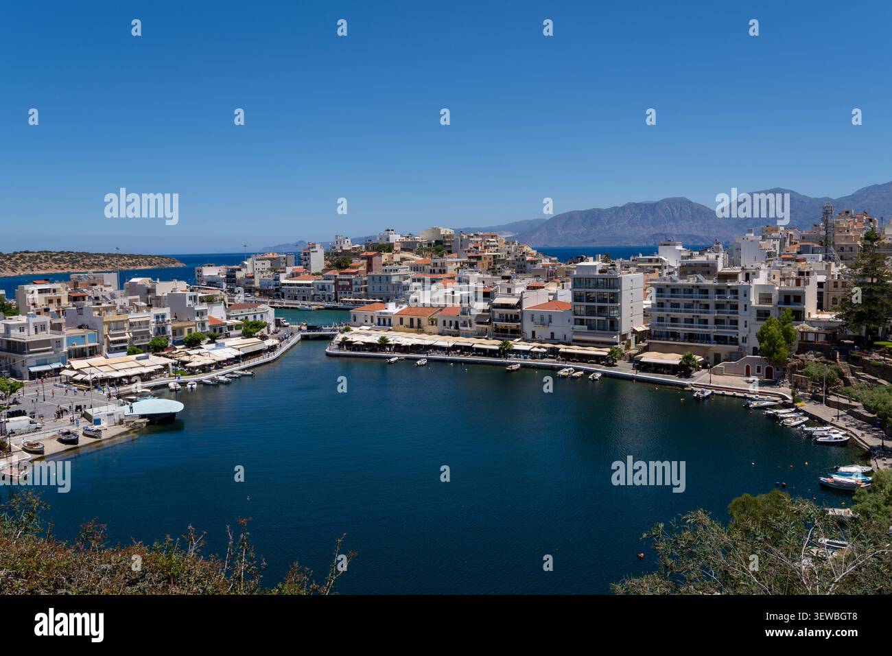 Un bellissimo panorama soleggiato di Agios Nikolaos a Creta, che mostra il bacino rotondo del Lago Voulismeni con ristoranti costeggiati sul lungomare, hotel, attraccati Foto Stock