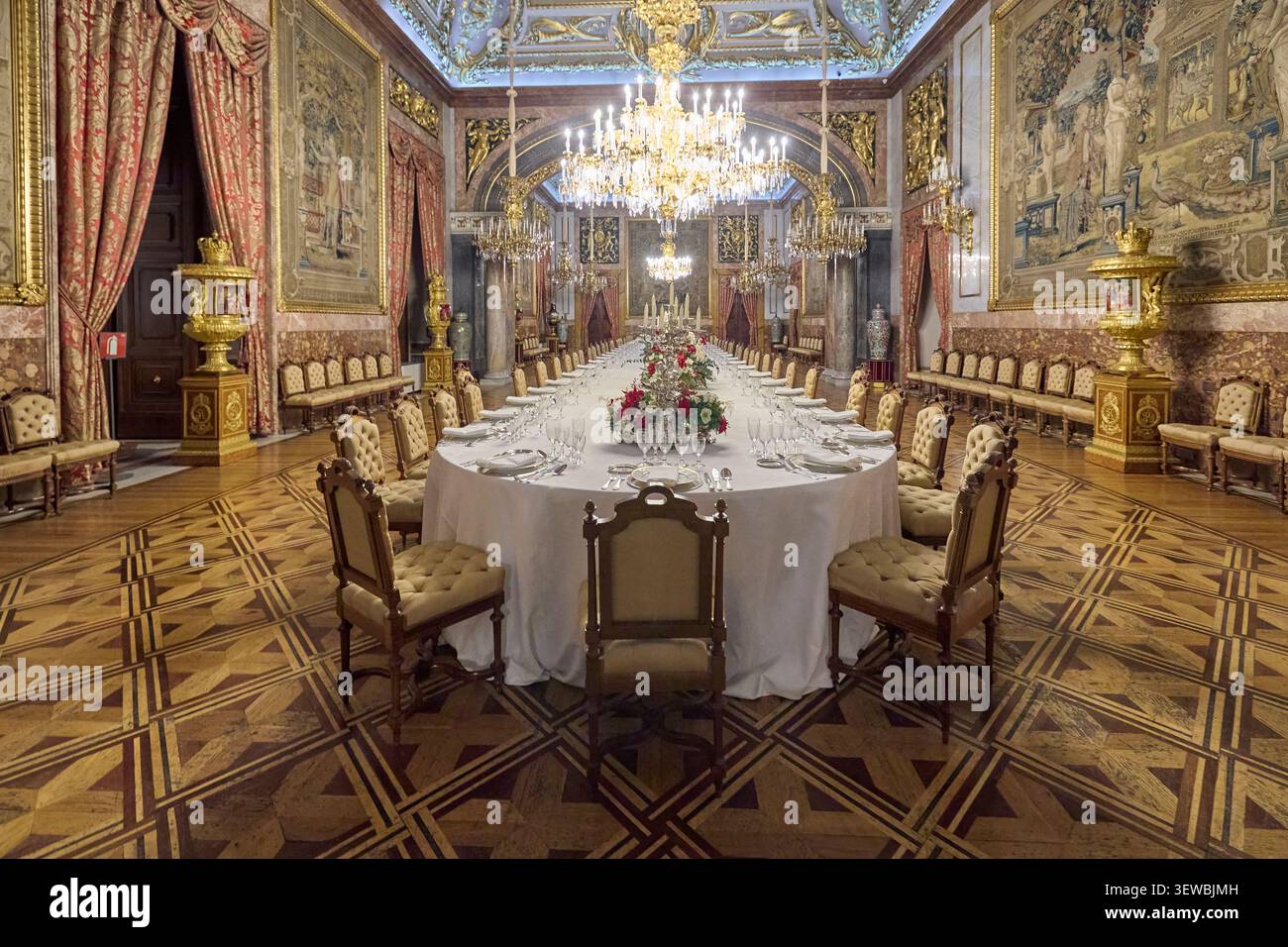 Elegante sala banchetti all'interno del Palazzo reale di Madrid con lungo tavolo da pranzo, lampadari e arazzi. Gli interni reali storici sono preparati per una cerimonia formale Foto Stock
