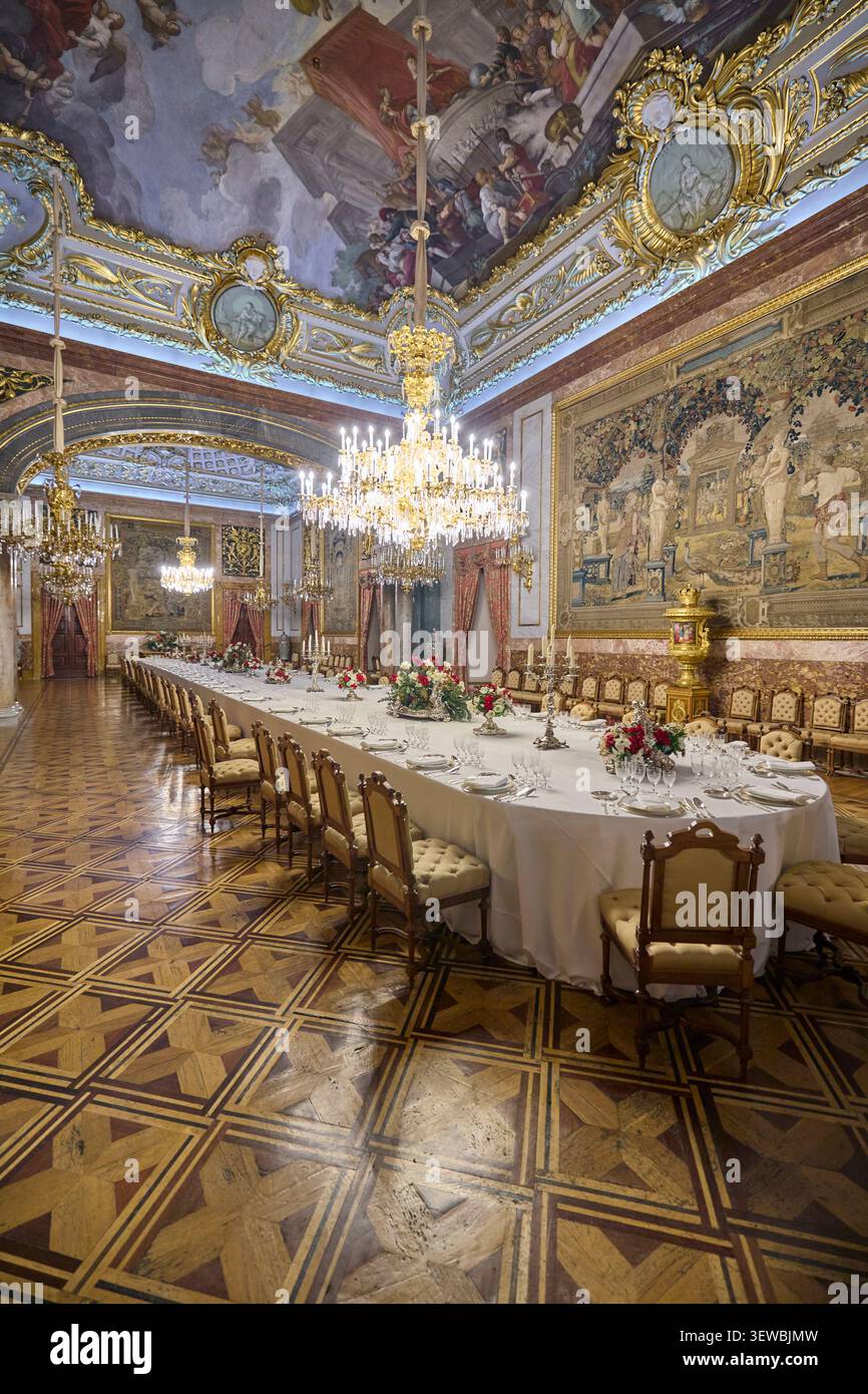 Elegante sala banchetti all'interno del Palazzo reale di Madrid con lungo tavolo da pranzo, lampadari e arazzi. Gli interni reali storici sono preparati per una cerimonia formale Foto Stock