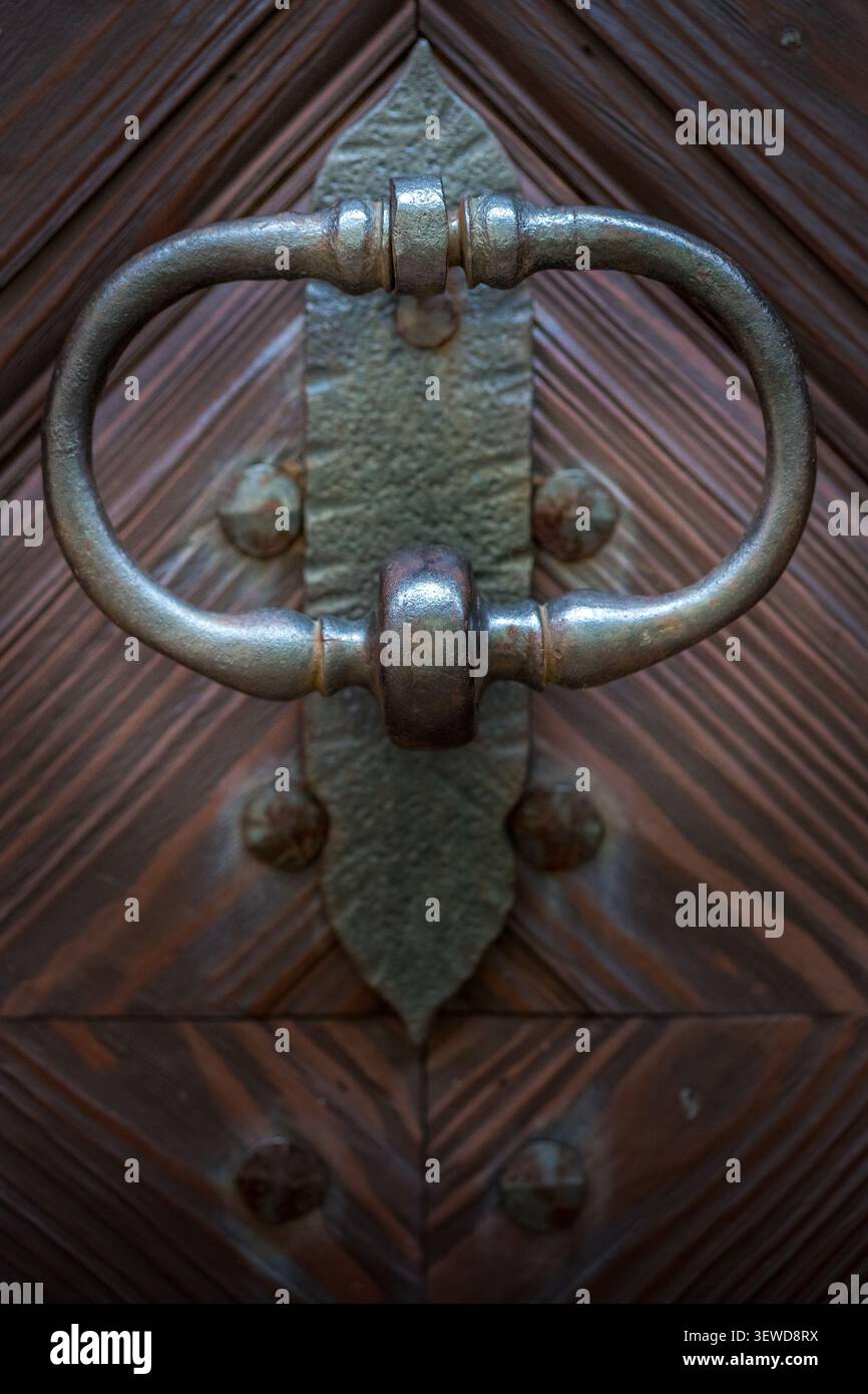 Porta a battente ad anello in ferro battuto tradizionale montata su una porta storica in legno con motivo geometrico a grana. Foto Stock
