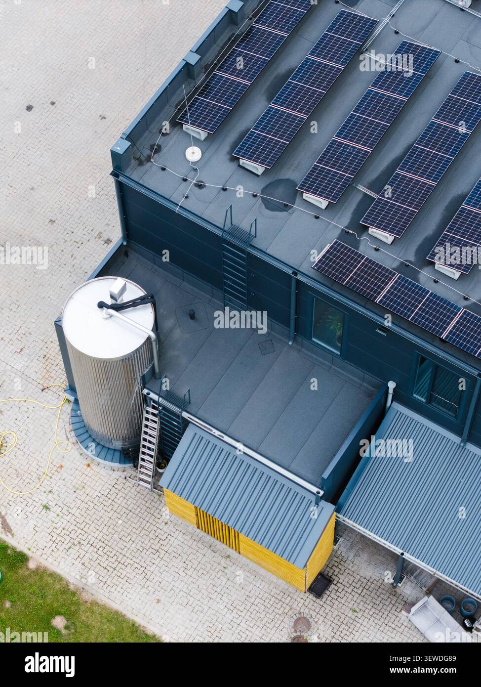Vista aerea di un edificio di una fabbrica di formaggi con pannelli solari sul tetto, un grande silo in metallo e una piccola struttura dal tetto giallo a Ikskile, Ogre Munic Foto Stock