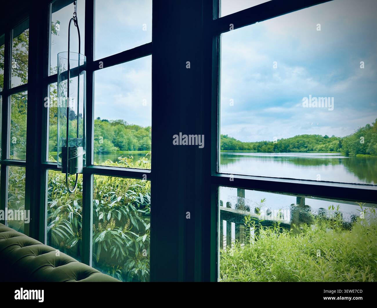 Una vista sul lago circondata da alberi attraverso finestre con cornici in acciaio che si affacciano sulla piscina Bracebridge nel Sutton Park. - Immagine stock catturata con smartphone