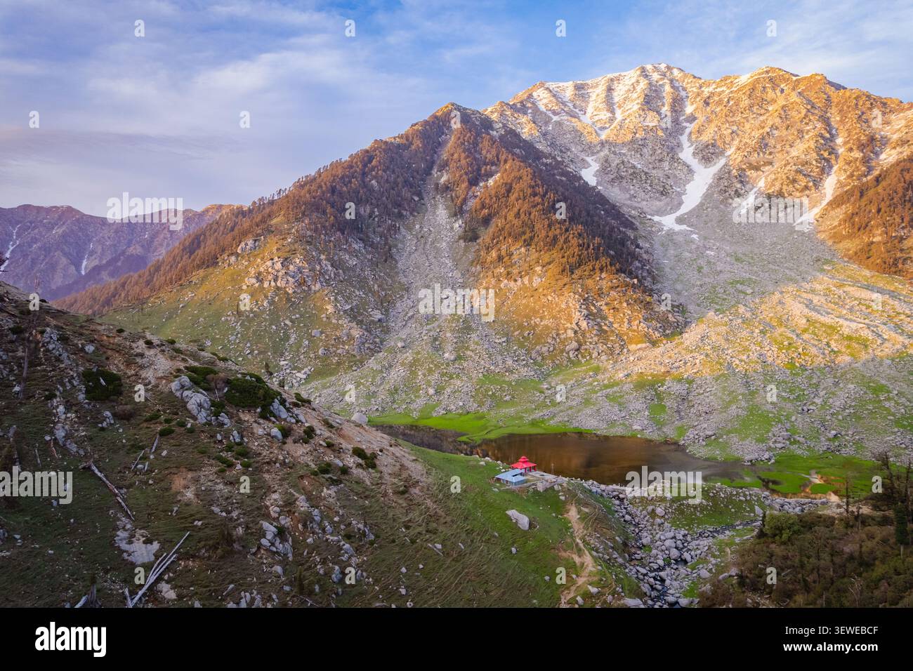 Vista aerea del lago Kareri Trek circondato da aspre montagne himalayane, pendii rocciosi e prati verdi lussureggianti sotto la luce dorata dell'alba a Ka Foto Stock