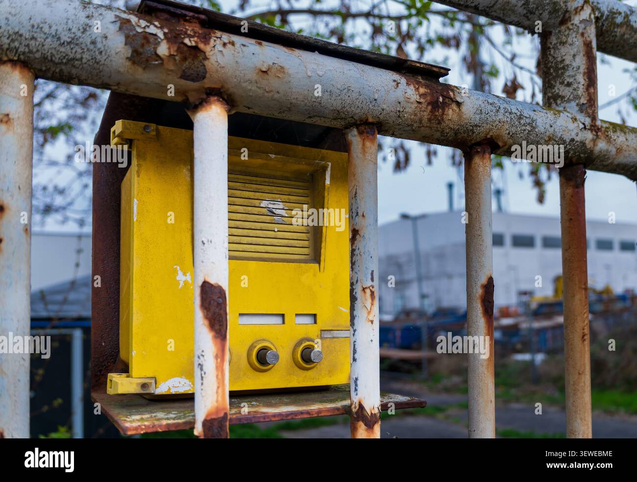 Vecchio interfono industriale giallo montato dietro una recinzione metallica arrugginita all'ingresso di un sito commerciale o industriale. Foto Stock