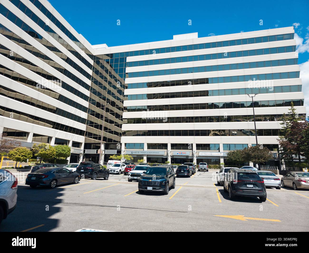 Un moderno ed elegante edificio per uffici commerciali con finestre in vetro riflettente, cartelli aziendali, aree verdi curate e un ingresso accessibile al 305 Mil - Immagine stock catturata con smartphone