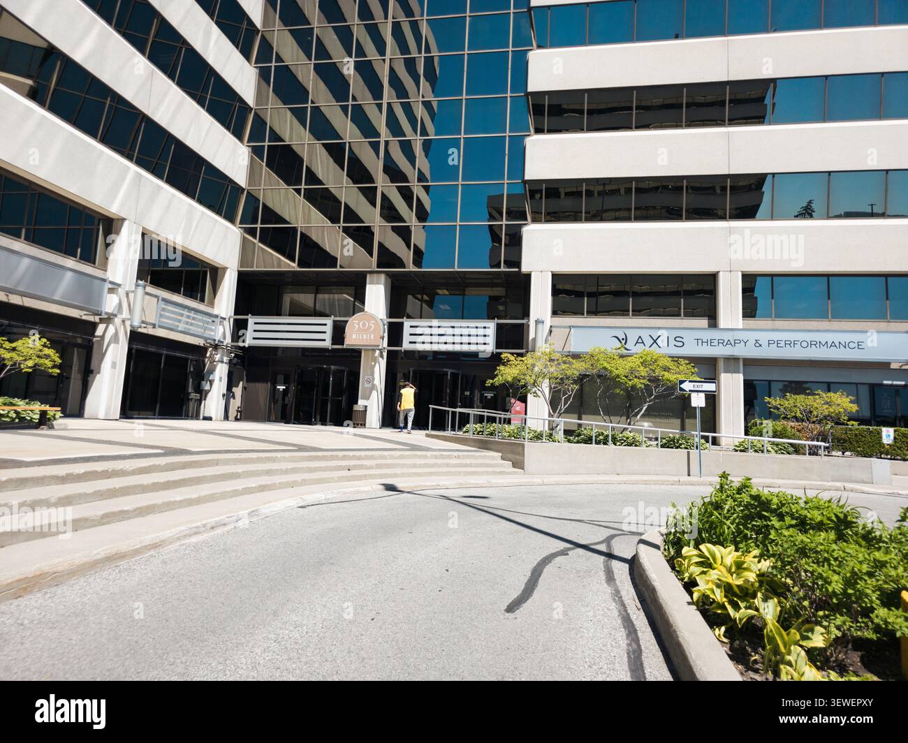 Un moderno ed elegante edificio per uffici commerciali con finestre in vetro riflettente, cartelli aziendali, aree verdi curate e un ingresso accessibile al 305 Mil - Immagine stock catturata con smartphone