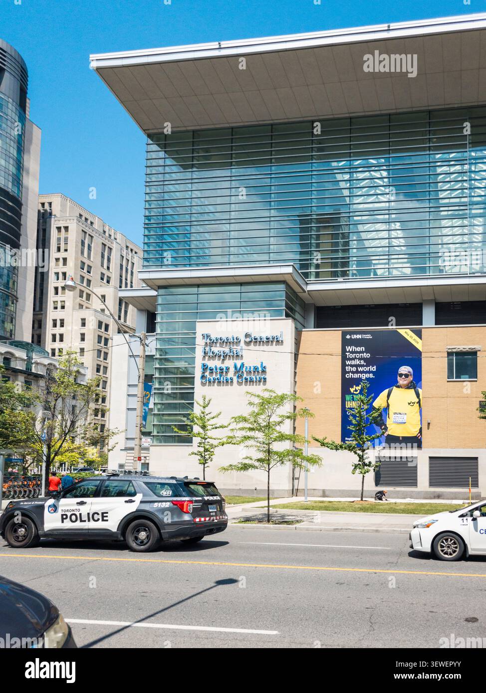 Il Centro Cardiaco Peter Munk del Toronto General Hospital si trova lungo una strada trafficata del centro città, caratterizzato dalla sua moderna facciata in vetro, un grande banner promozionale - Immagine stock catturata con smartphone