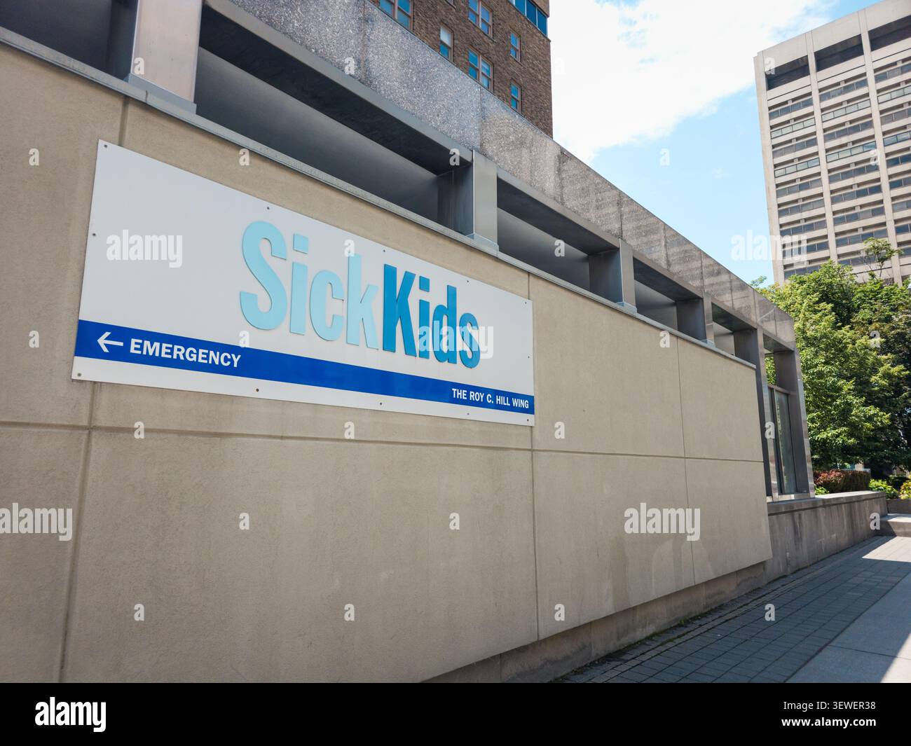 Una vista chiara dell'esterno dell'ospedale SickKids mostra il cartello blu per le emergenze sull'ala Roy C. Hill, sullo sfondo degli edifici urbani circostanti - Immagine stock catturata con smartphone