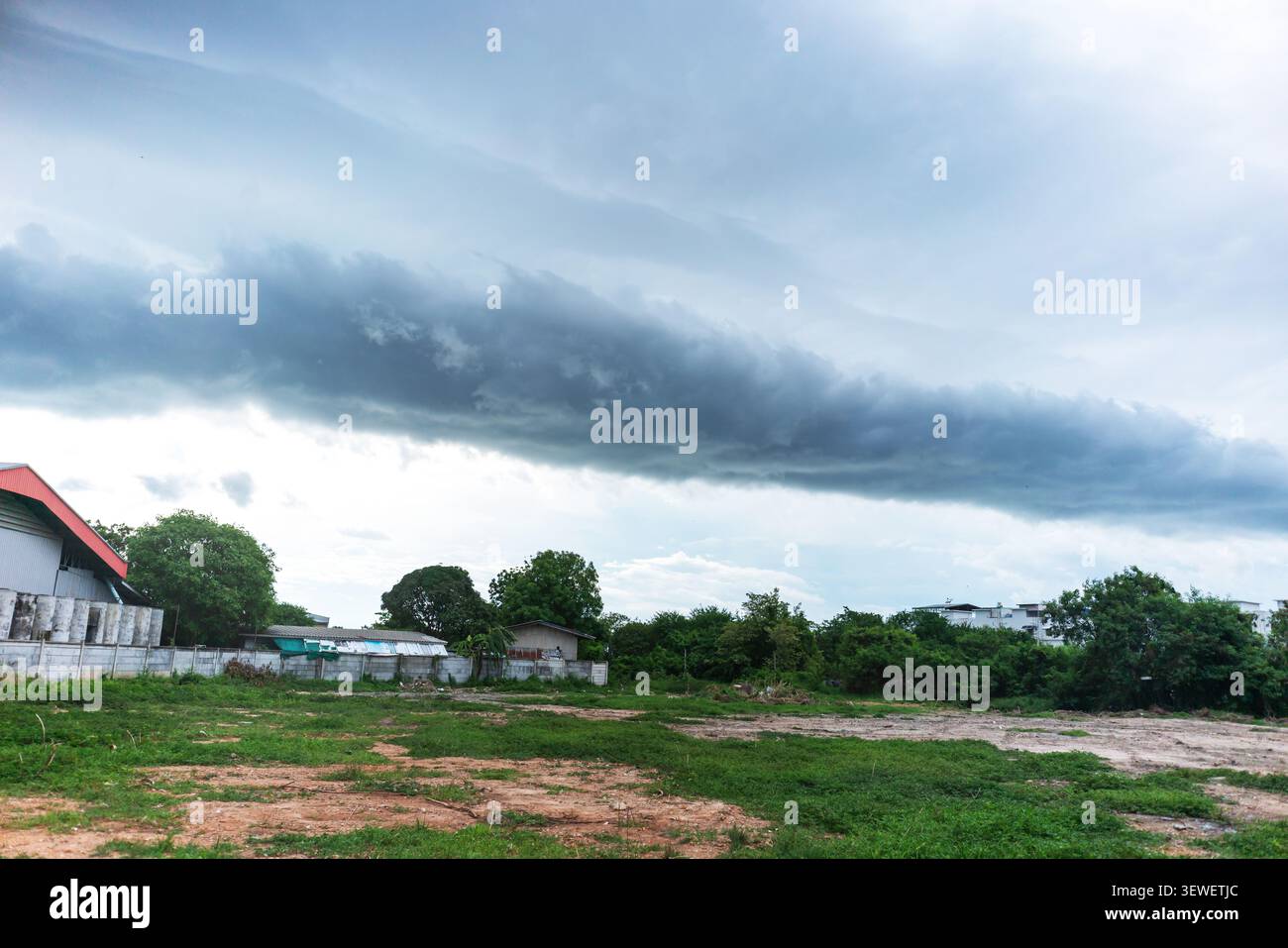 Un paesaggio caratterizzato da spettacolari nuvole scure che coprono il cielo su un campo verde con alberi ed edifici sparsi, evidenziando una giornata ricoperta in un r Foto Stock