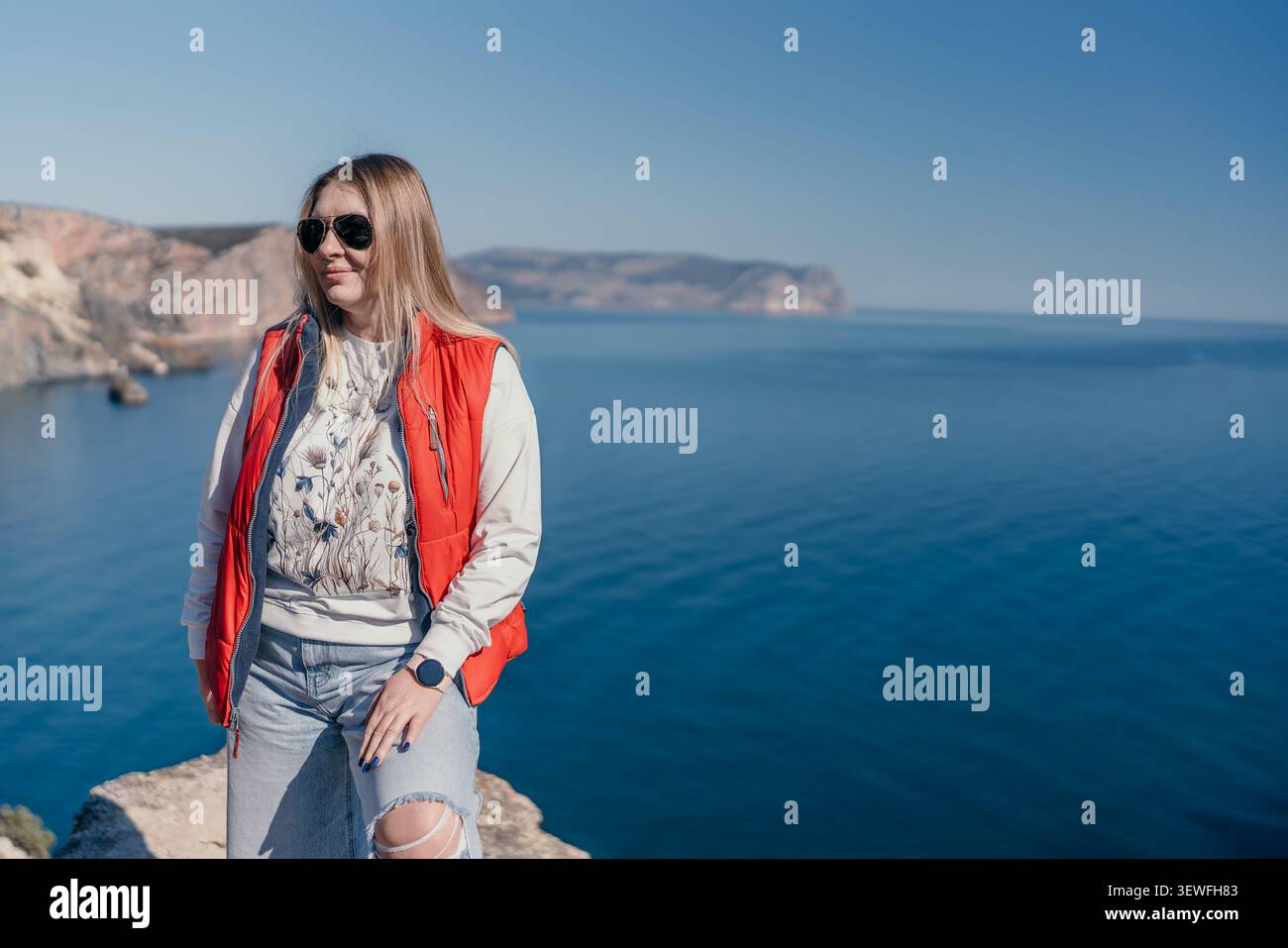 Donna scogliera dell'oceano in piedi in un gilet rosso e occhiali da sole su un'alta parete rocciosa con spazio per copiare i viaggi e l'avventura Foto Stock