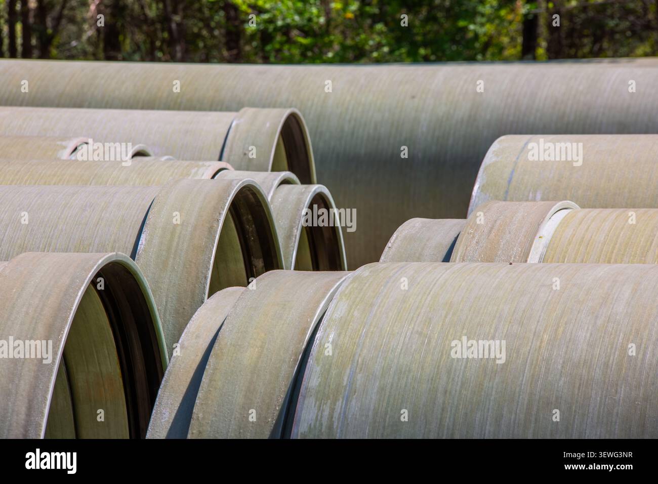 Sezioni di tubi industriali impilate con estremità preparate su supporti in cantiere all'aperto, pronte per l'installazione di tubazioni Foto Stock
