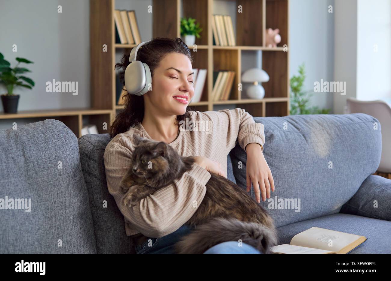 Donna che si rilassa a casa con il gatto, indossa le cuffie e ascolta la musica sul divano Foto Stock