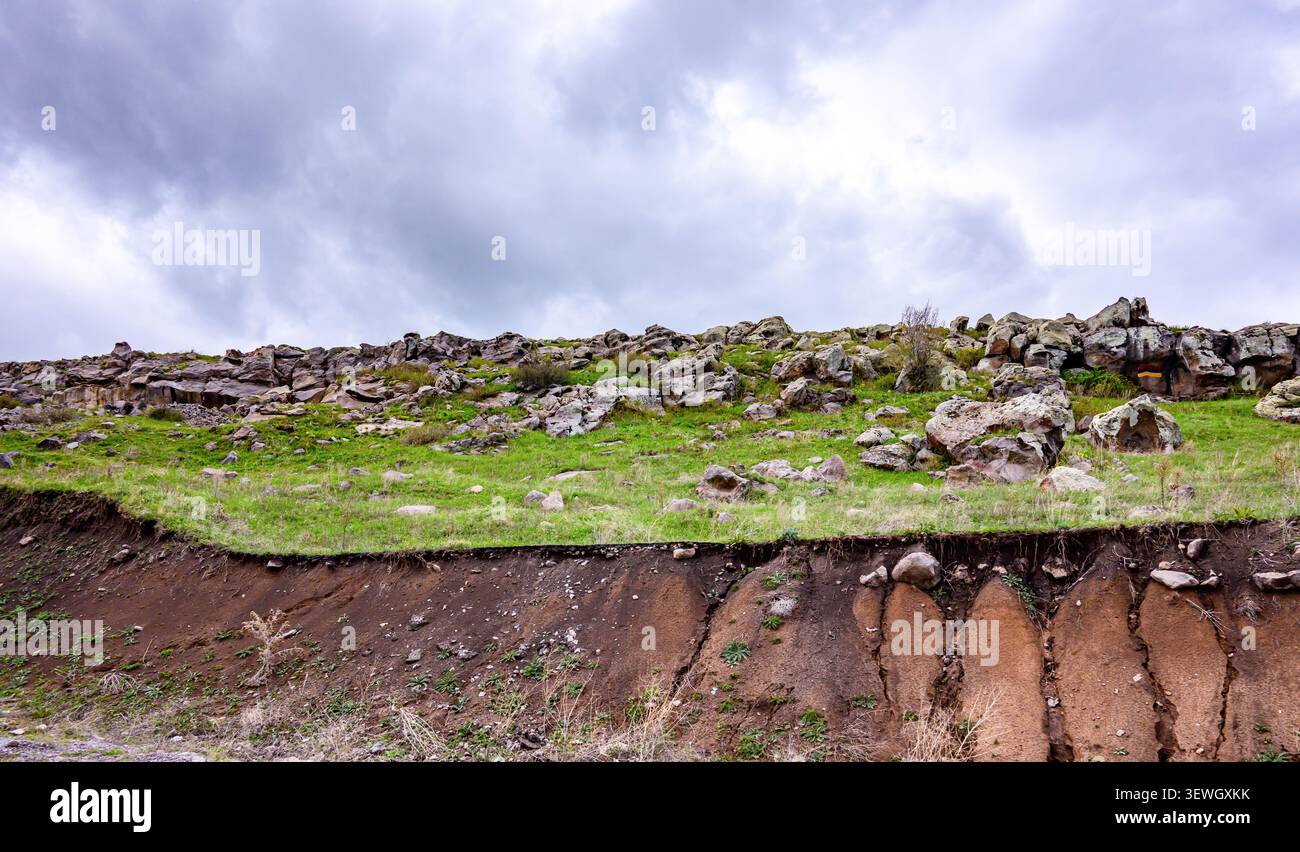 Pendio erboso con terreno esposto e rocce sparse sotto il cielo nuvoloso Foto Stock