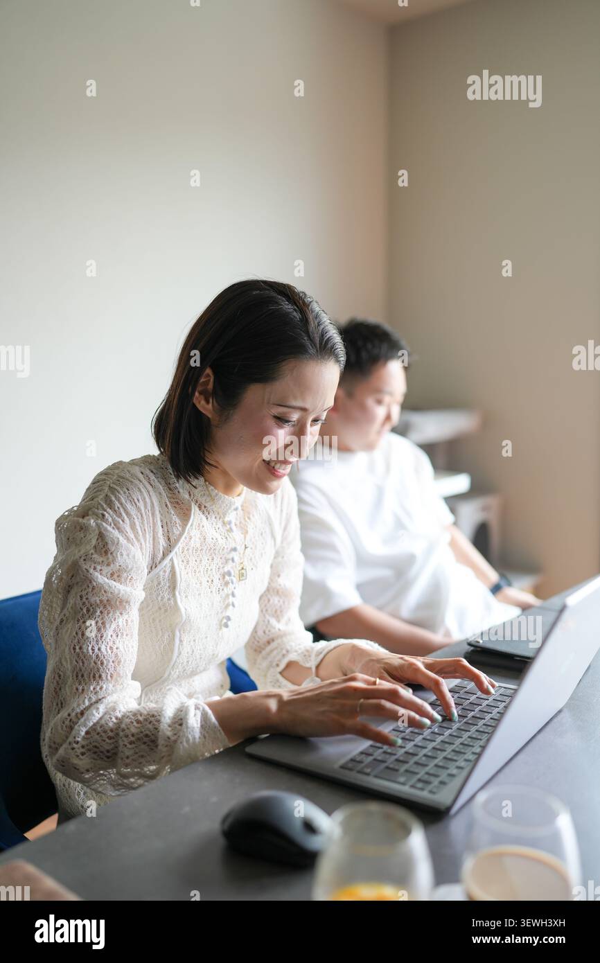 La luce soffusa illumina una donna concentrata che digita su un notebook. La sua espressione calma suggerisce concentrazione e scopo. L'uomo siede tranquillamente dietro di lei, anche e Foto Stock
