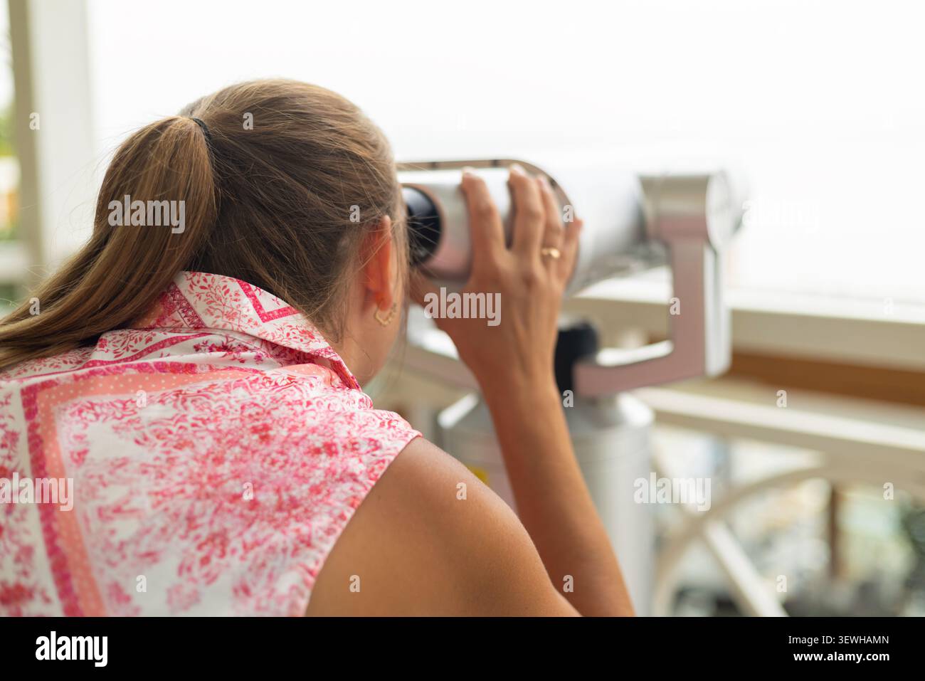 Donna con coda di cavallo che usa il telescopio pubblico Foto Stock