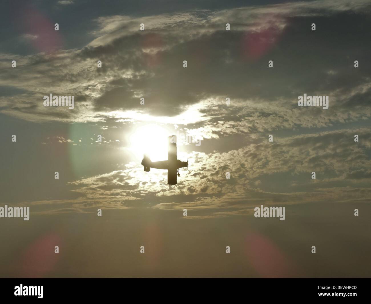 Aeroplano che vola creando una silhouette contro il sole luminoso al tramonto con nuvole discontinue Foto Stock