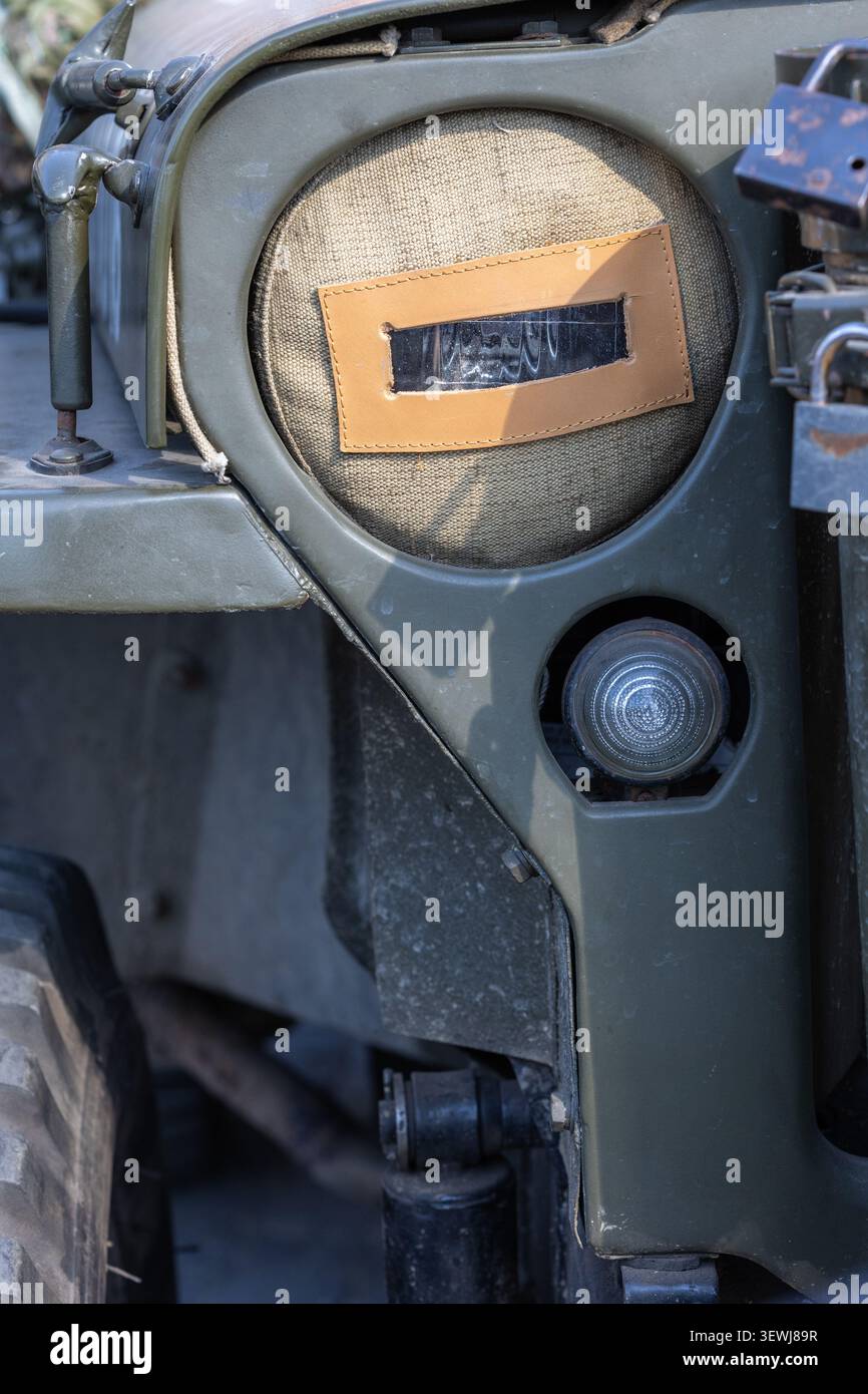 Primo piano dettagliato di un veicolo militare vintage verde oliva caratterizzato da un rivestimento in tessuto per fari oscuranti con fessura in pelle, luce secondaria e heav Foto Stock