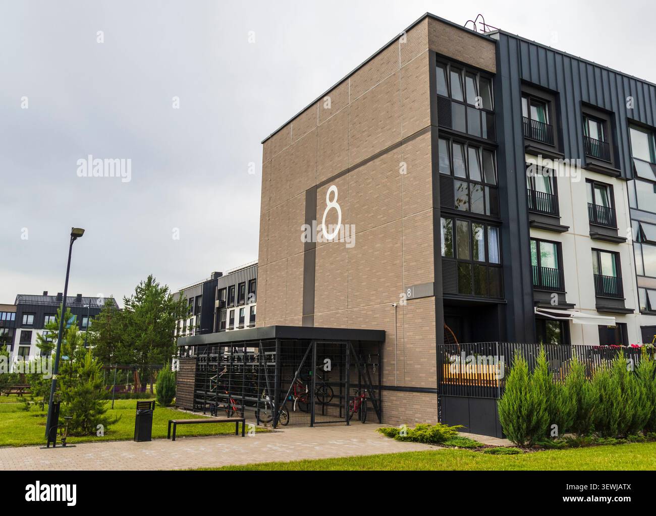Moderno edificio residenziale con rivestimento in mattoni, un'evidente grafica bianca numero otto e un sicuro armadietto di stoccaggio per biciclette in metallo nero. Foto Stock