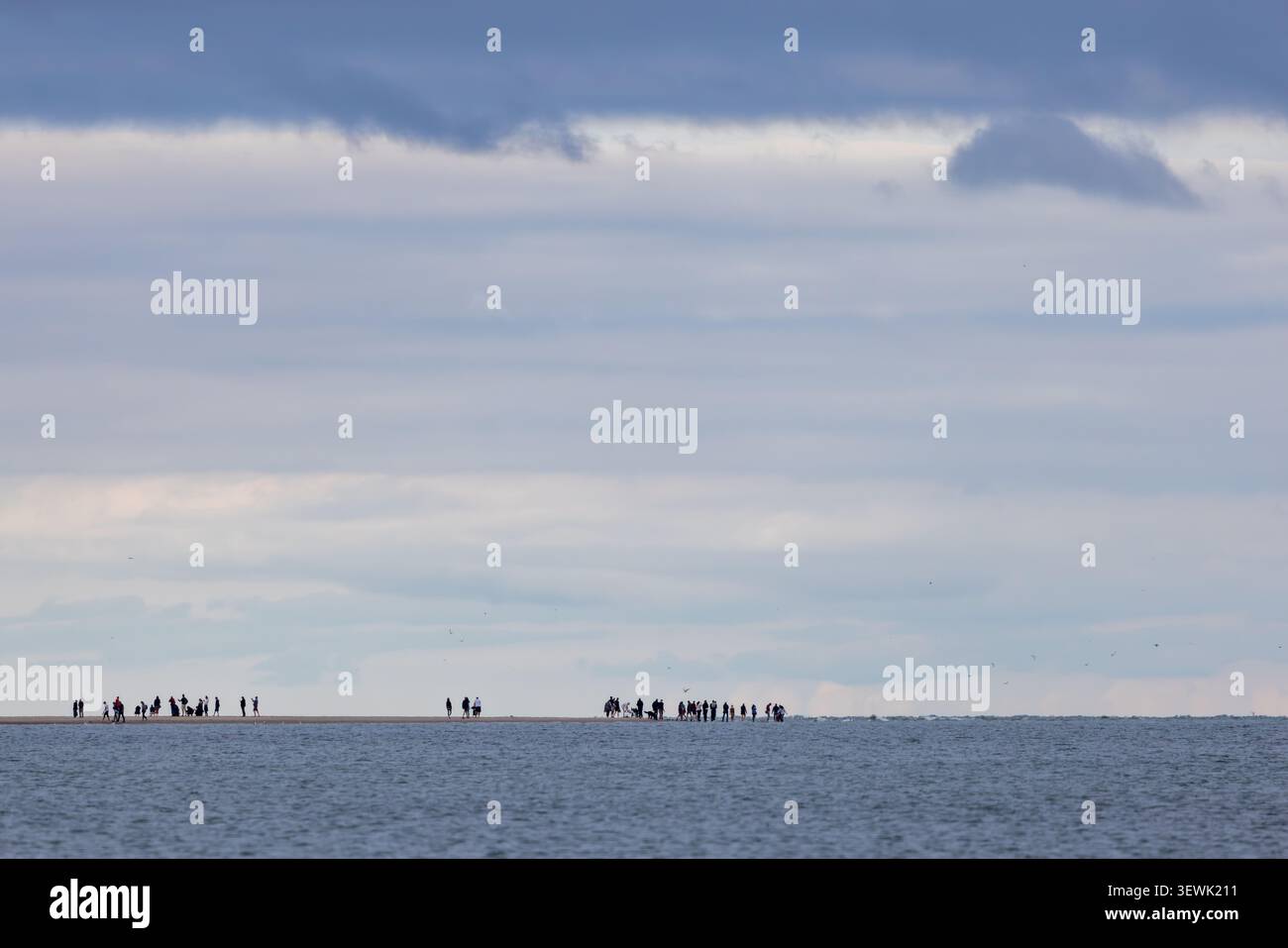 Gli amanti della spiaggia silenziosi si trovano sulla costa lontana. Il cielo trattiene morbide nuvole, un mare calmo. La gente guarda fuori, perduta nella contemplazione tranquilla. Perfetto per i viaggi, Foto Stock