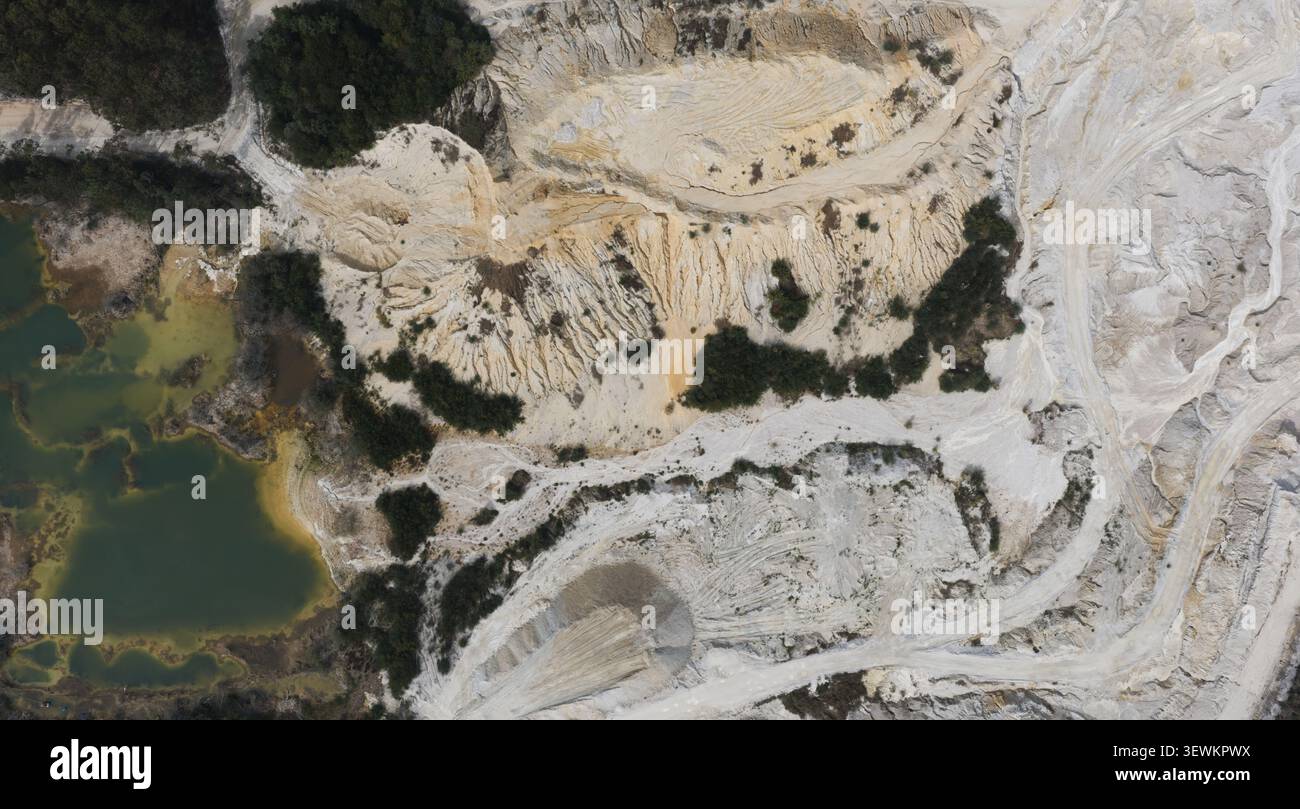 Portogallo - 25 giugno 2026: Veduta aerea di una laguna mineraria di cava con acqua turchese, terreno sabbioso esposto e profondi segni di scavo circondati dal verde Foto Stock