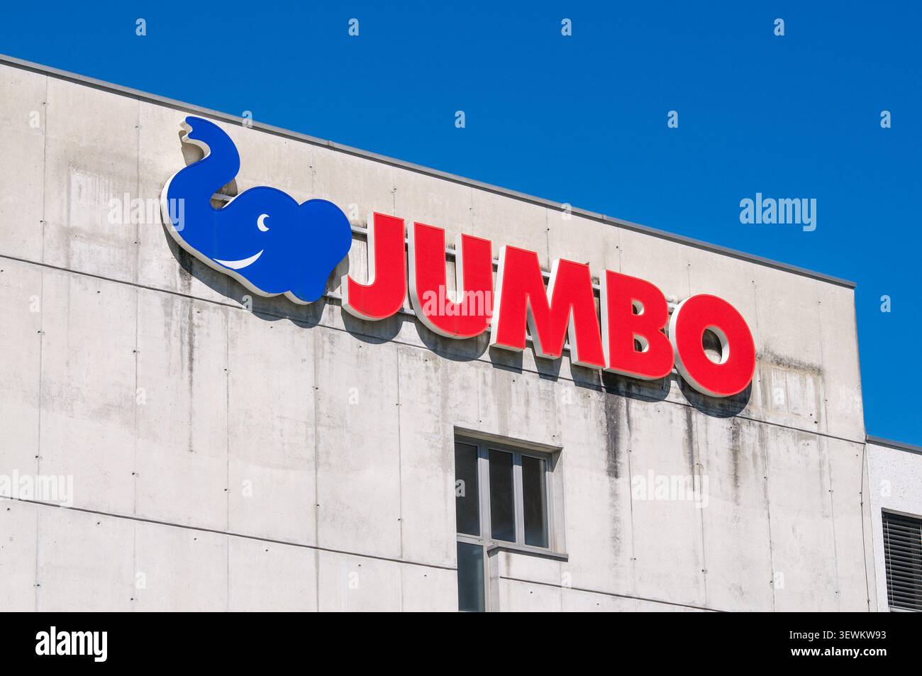 Mendrisio, Ticino, Svizzera - 3 giugno 2026: Vista ad angolo basso del cartello ufficiale del negozio Jumbo con il logo dell'elefante blu su una facciata in cemento. Jumb Foto Stock