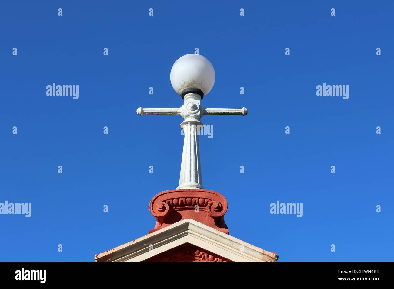Lampada da strada vintage Heritage con lampada a globo bianca sulla parte superiore di un tetto architettonico decorato contro un cielo blu Foto Stock