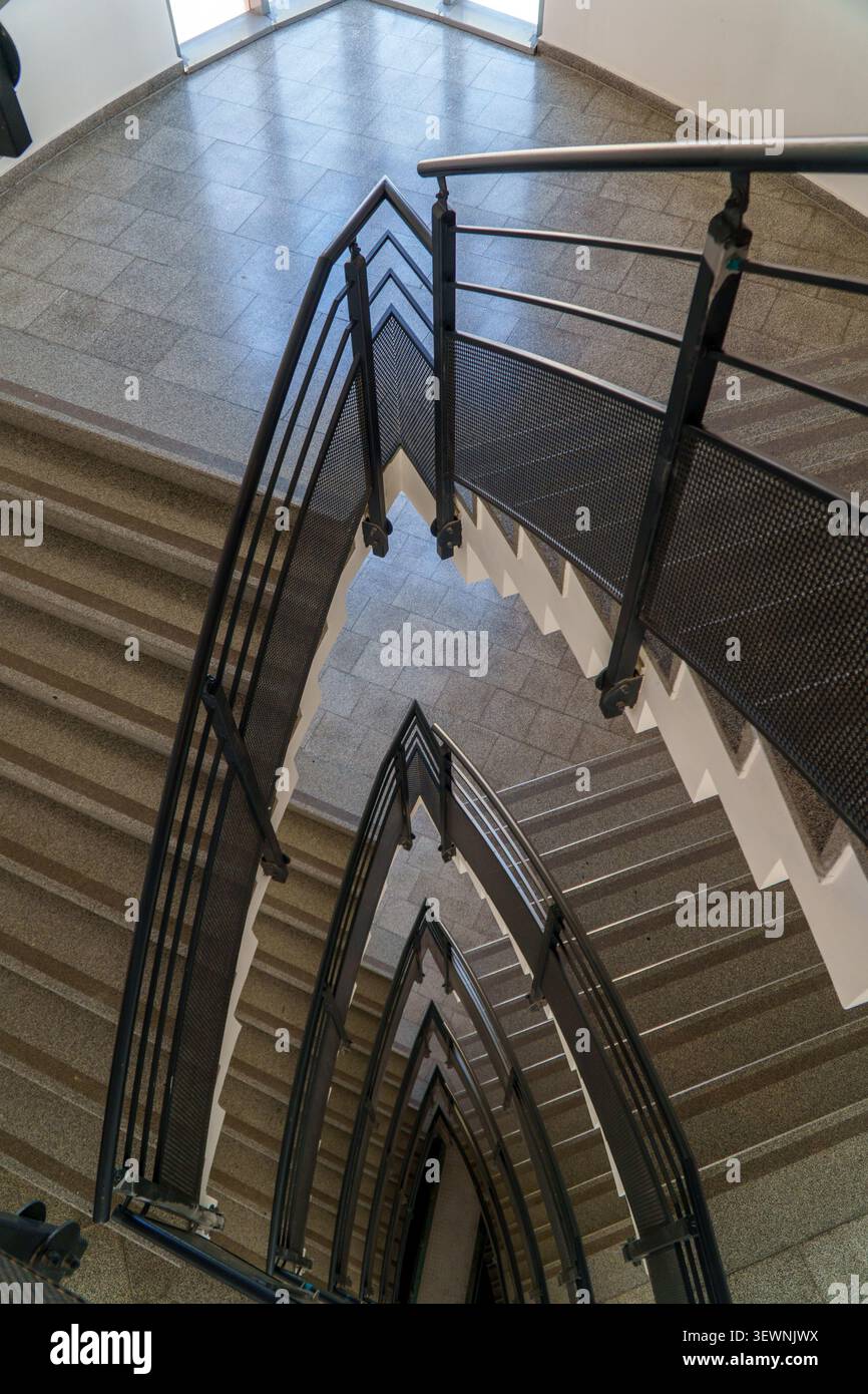 Una vista ad alto angolo che si affaccia su una scala moderna con ringhiere in mesh di metallo scuro che creano ripetuti motivi triangolari e linee geometriche. Foto Stock