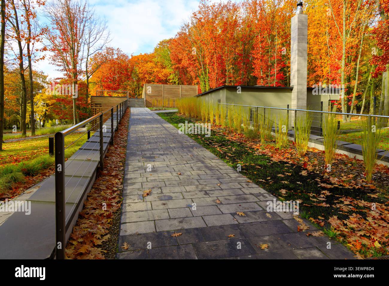 Un sentiero pavimentato conduce attraverso una piazza del parco adornata da fogliame arancione ardente ed elementi di costruzione contemporanei Foto Stock