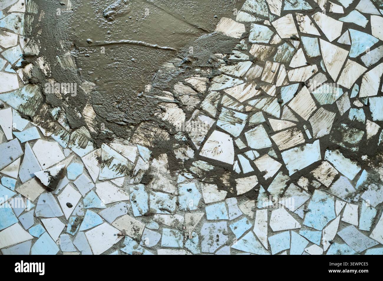 Piastrelle di ceramica rotte che formano un mosaico ruvido con cemento fresco. Rifacimento dei vecchi materiali. Ristrutturazione del pavimento in mosaico fai da te Foto Stock