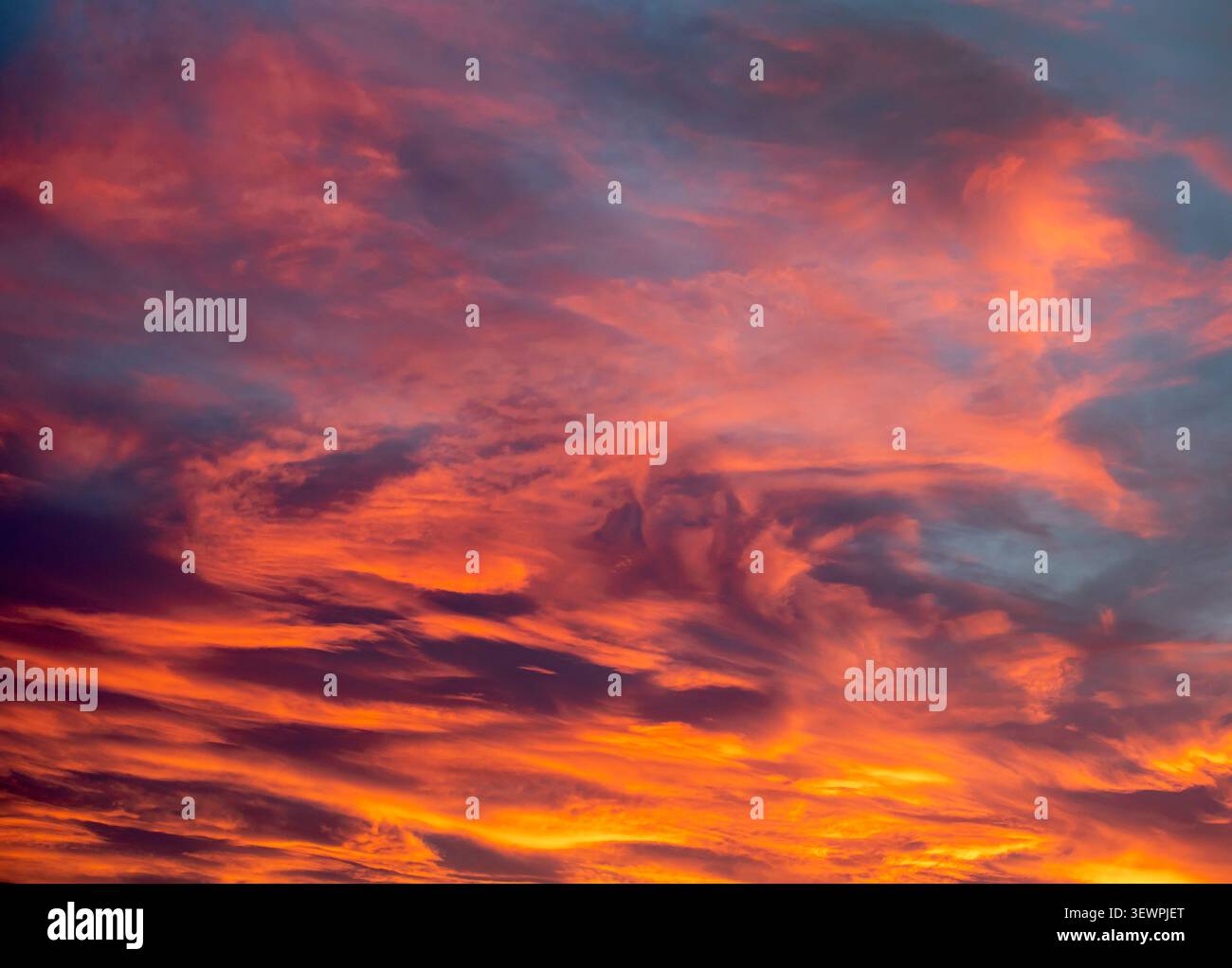 Il tramonto dipinge nuvole alla deriva in sfumature luccicanti di rosa viola e oro nel cielo serale Foto Stock