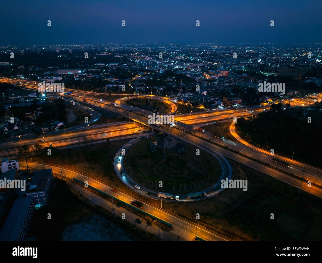 Uno svincolo stradale circolare illuminato di notte con vivaci percorsi luminosi dei veicoli in movimento a si racha chonburi in thailandia. Foto Stock