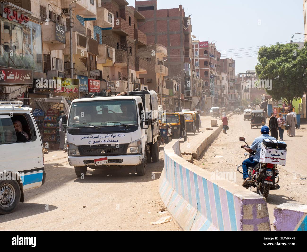 Veicoli e pedoni che si muovono lungo una strada polverosa in una città del Medio Oriente Foto Stock