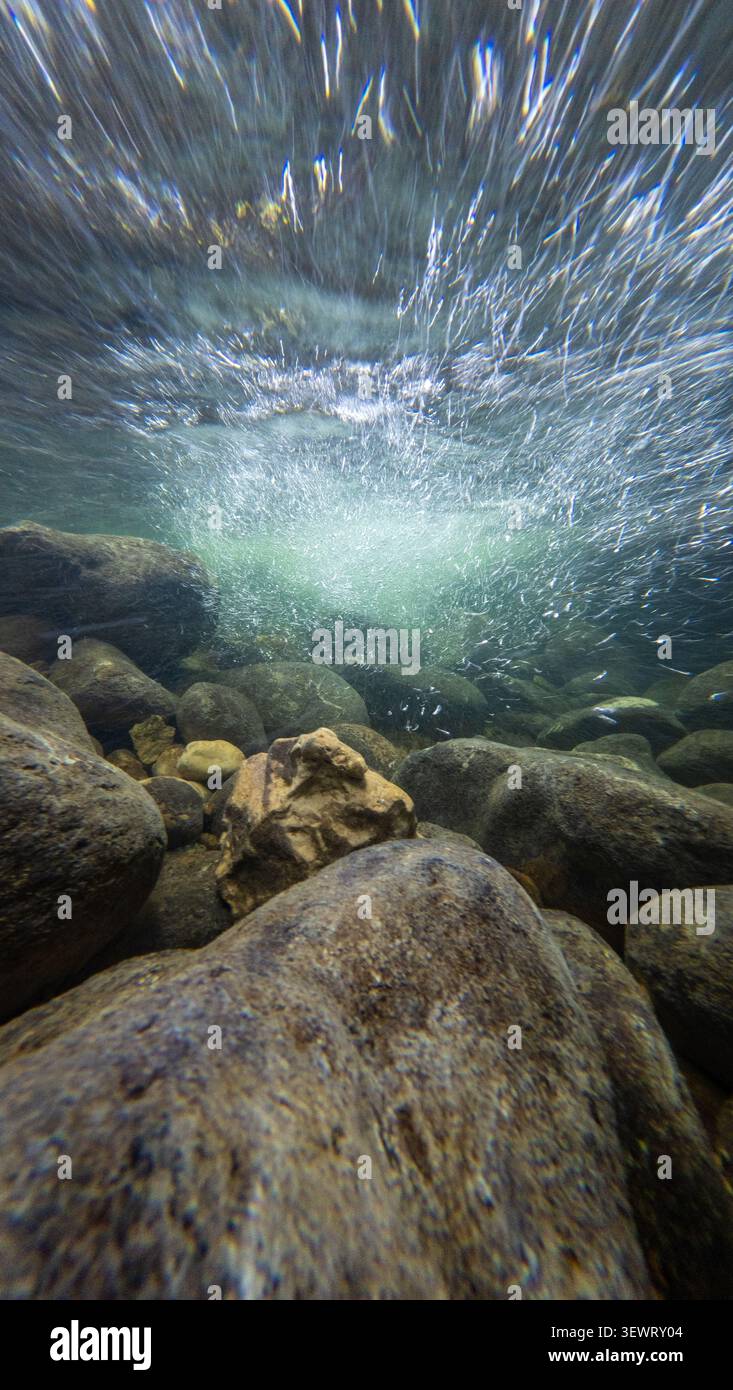 Vista subacquea in un selvaggio fiume di montagna svizzero che guarda verso la superficie turbolenta sotto una piccola cascata naturale, con forte corrente, bolle Foto Stock